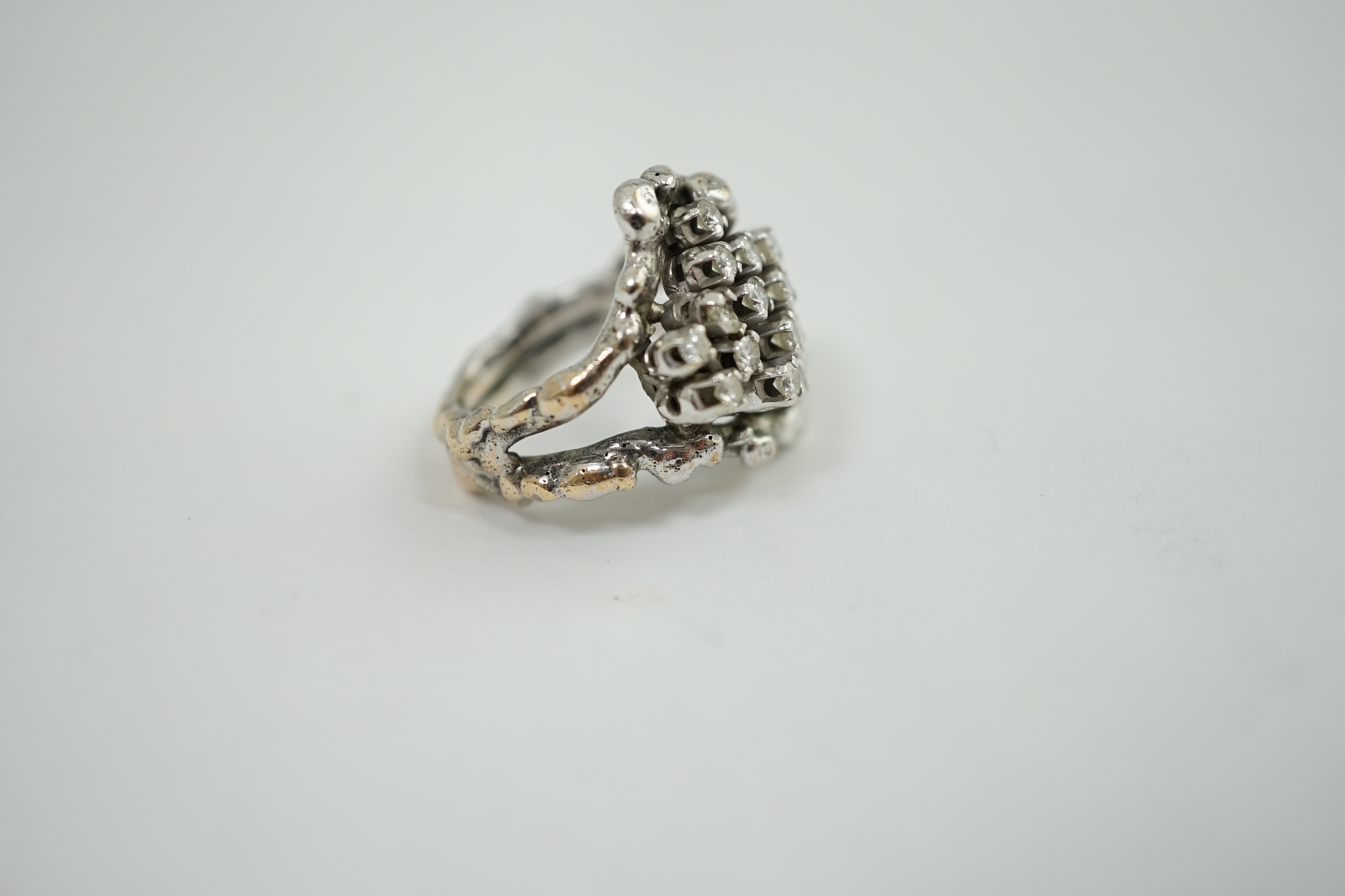 A modernist cast unmarked white metal dress ring, claw set with twenty small diamonds